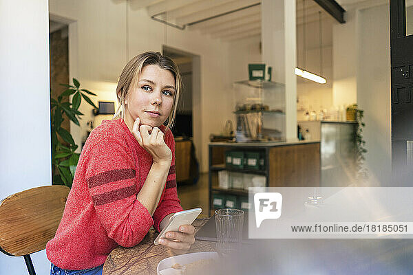 Contemplative freelancer with hand on chin sitting at table in cafe