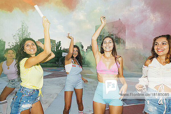 Smiling woman holding smoke torch standing with friends at sports court
