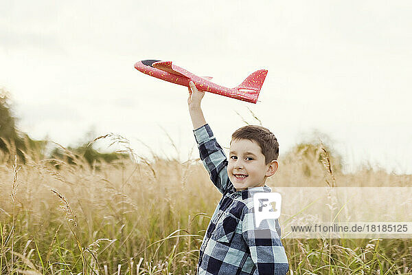Lächelnder süßer Junge  der mit einem Modellflugzeug auf dem Feld spielt