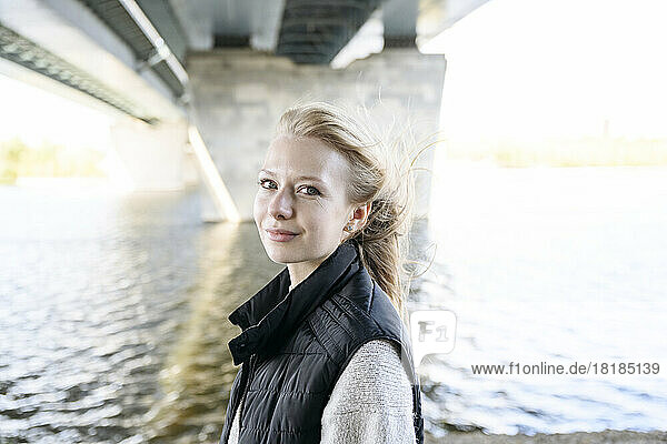 Smiling blond woman under bridge at river