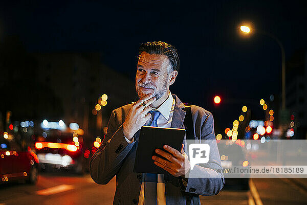 Thoughtful mature businessman standing with tablet PC on street