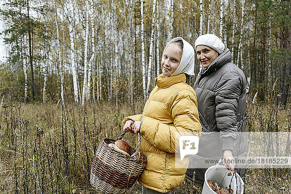 Smiling girl with grandmother collecting mushrooms in forest
