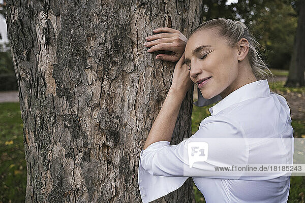 Smiling woman with eyes closed leaning on tree