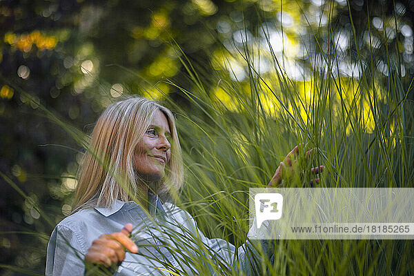 Mature woman with blond hair touching plant in garden