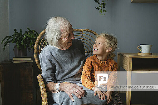 Happy grandmother and granddaughter looking at each other on chair