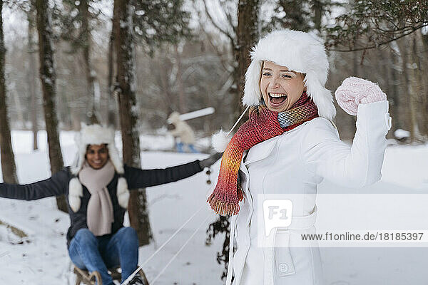 Happy woman flexing muscles with man sitting on sled in snow
