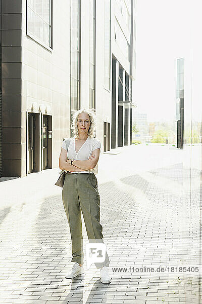 Businesswoman standing with arms crossed on footpath in front of building