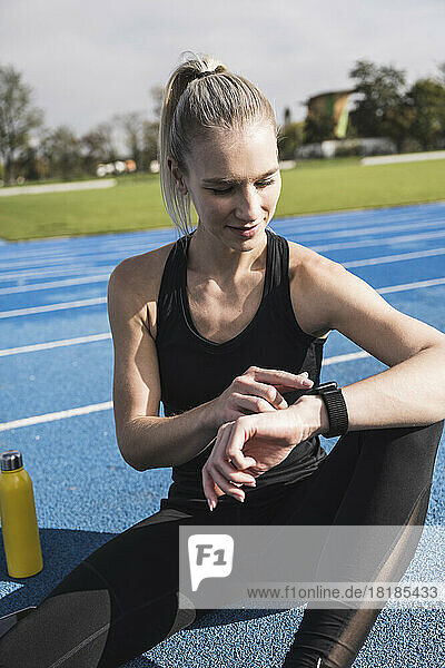 Young sportswoman using smart watch on track