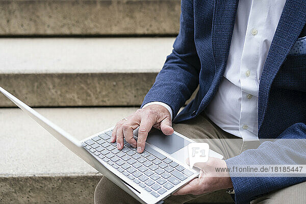 Businessman using laptop sitting on staircase