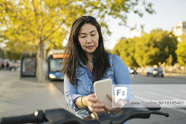 Reife Frau mietet per Smartphone auf dem Fußweg ein Fahrrad