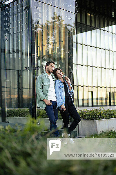 Couple leaning on glass wall of building