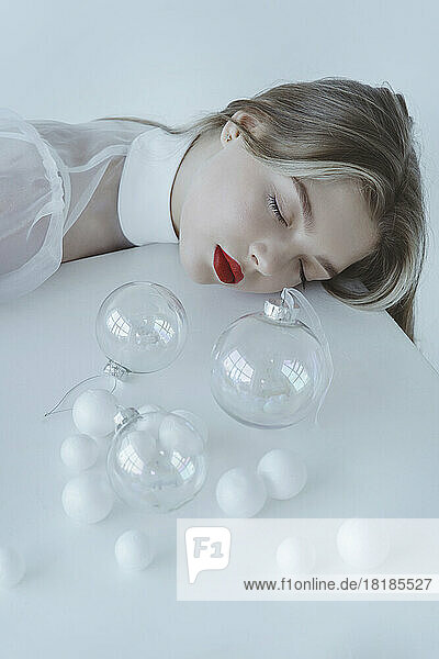 Beautiful girl with eyes closed sleeping by Christmas balls on table