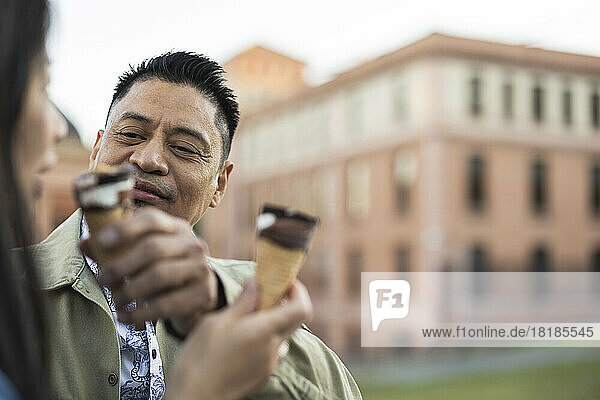 Smiling mature man feeding ice cream cone to woman