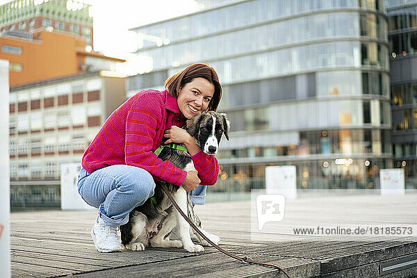 Smiling woman embracing dog crouching on pier