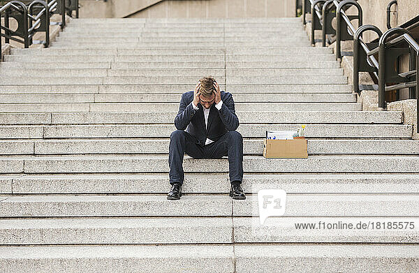 Besorgter Geschäftsmann sitzt mit Karton auf der Treppe