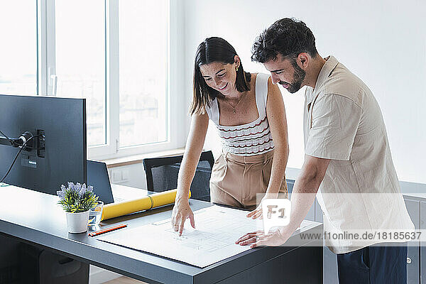 Young architect with colleague discussing blueprint in office