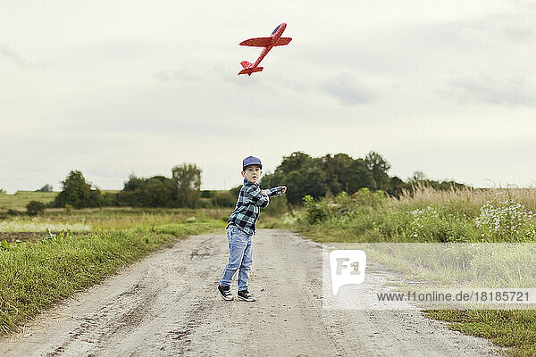 Cute boy flying toy airplane on dirt road