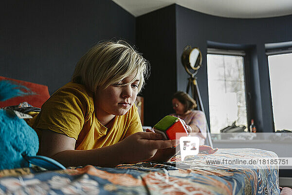 Boy playing with puzzle cube lying on bed at home