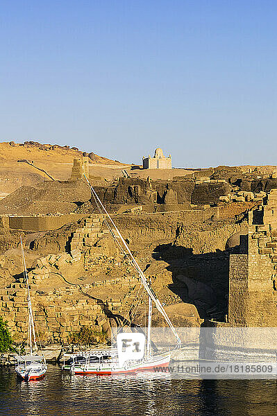 Egypt  Aswan Governorate  Aswan  Sailboats floating on bank of Nile river with Mausoleum of Aga Khan in background