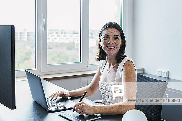 Happy young graphic designer using laptop in office