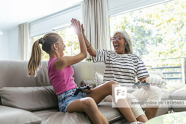 Cheerful senior woman giving high-five to granddaughter playing video game at home