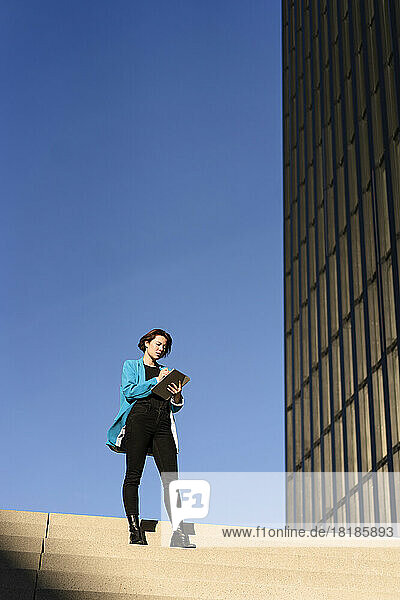 Businesswoman using tablet PC standing on staircase in front of blue sky