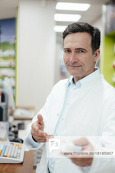 Smiling pharmacist showing medicine at store
