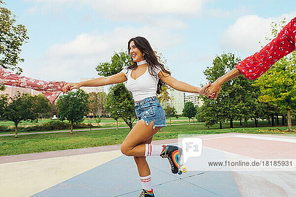 Happy young woman holding hands of friends and roller skating at sports court