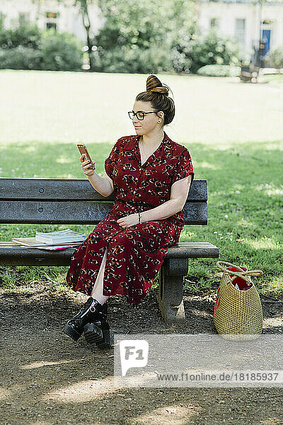 Woman with bun sitting on bench looking at cell phone