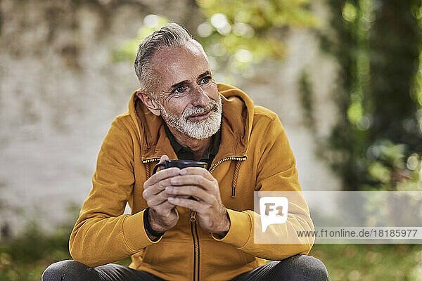 Smiling mature man sitting with coffee cup at park