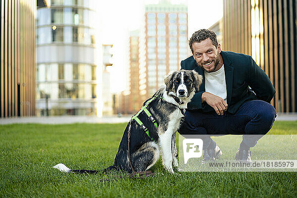 Smiling businessman with pet dog crouching on grass