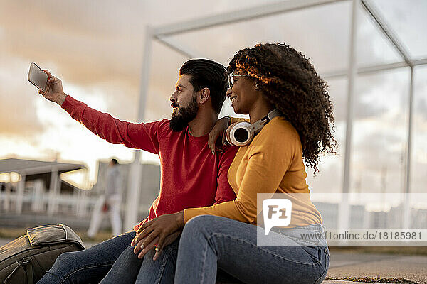 Happy woman with man taking selfie through smart phone at sunset