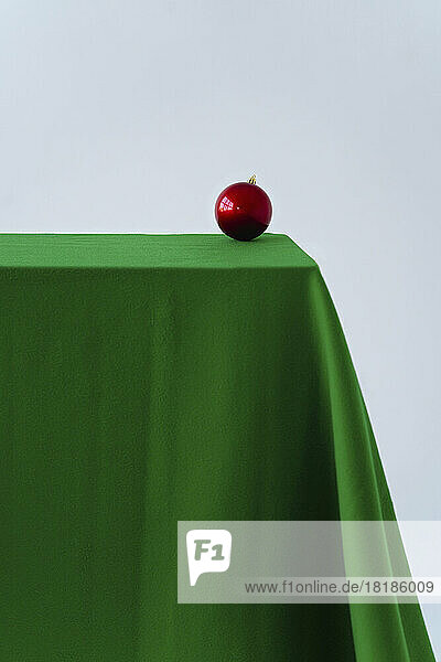 Red Christmas ornament on green velvet tablecloth against white background