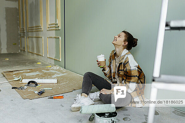 Young woman with disposable coffee cup laughing in apartment