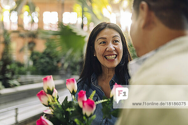 Happy mature woman with flowers looking at boyfriend on Valentine's Day