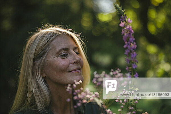 Smiling woman looking at flowering plant in garden
