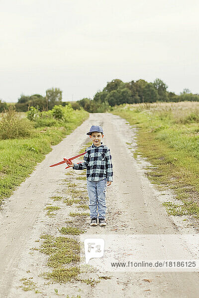 Netter Junge mit Mütze hält Modellflugzeug auf unbefestigter Straße