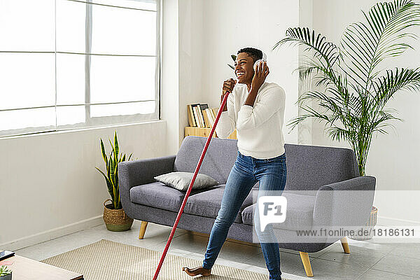 Carefree woman sweeping the floor and listening to music with headphones at home