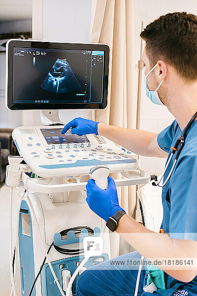 Young doctor examining and operating ultrasound machine at hospital