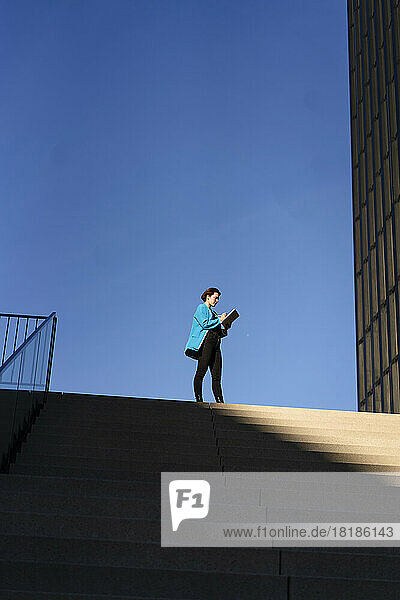 Businesswoman standing near steps with clear blue sky in background
