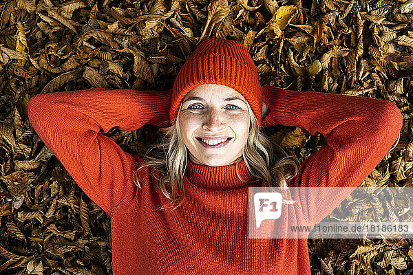 Lächelnde reife Frau mit blauen Augen  die auf Herbstblättern liegt