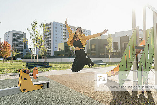 Fröhliche Frau springt an einem sonnigen Tag auf dem Spielplatz