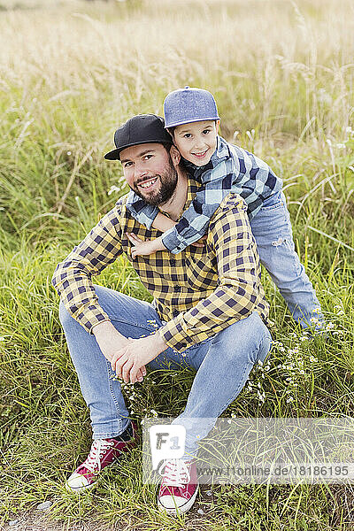 Boy embracing father from behind in meadow