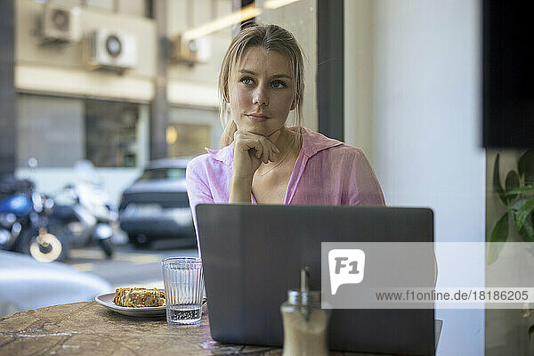 Thoughtful freelancer sitting with laptop in cafe