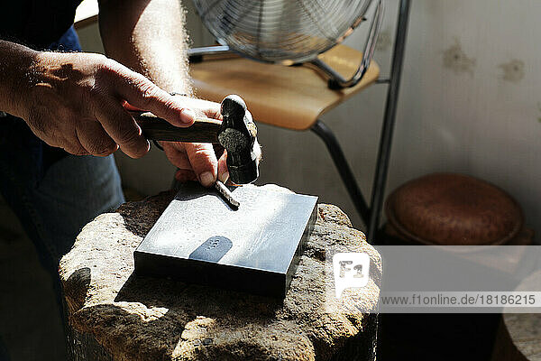 Jeweller hammering on metal to make jewelry in workshop