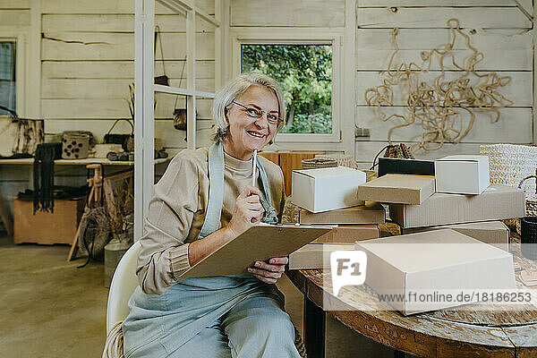 Happy craftswoman holding clipboard in workshop