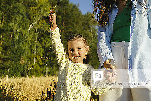 Girl holding hands with mother and standing at field on sunny day