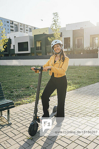 Glückliche junge Frau  die an einem sonnigen Tag mit einem Elektroroller steht