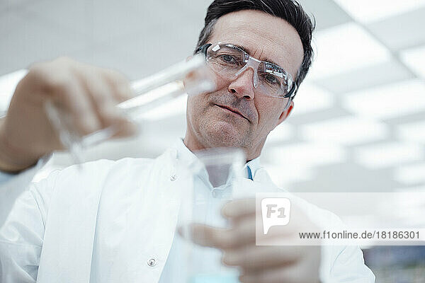 Chemiker gießt im Labor Chemikalien aus Reagenzglas in Kolben