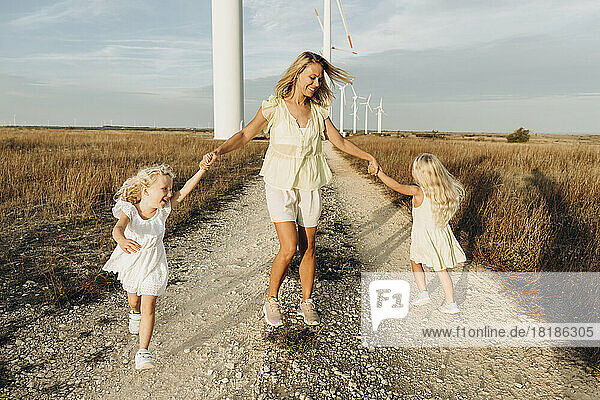 Cheerful woman enjoying and playing with daughters at field on sunny day